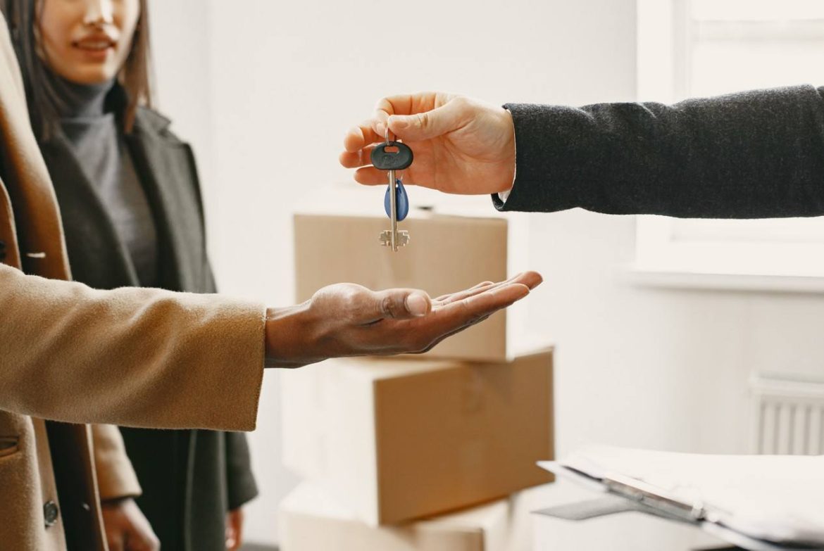 Remise de clés dans les mains d'un nouveau locataire après un déménagement dernière minute réussi, avec des cartons empilés en arrière-plan.
