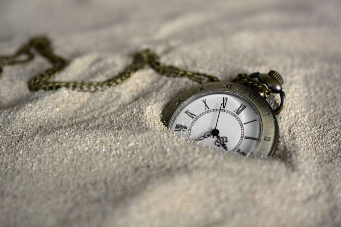 Une montre à gousset ancienne est partiellement enfouie dans du sable, symbolisant la nature du temps pour gérer le décalage horaire.