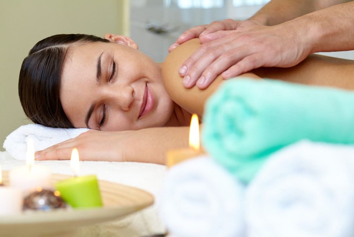 Femme souriante recevant un massage du dos sur une table de soin avec des bougies pour un massage gestion anxiété et stress chronique.