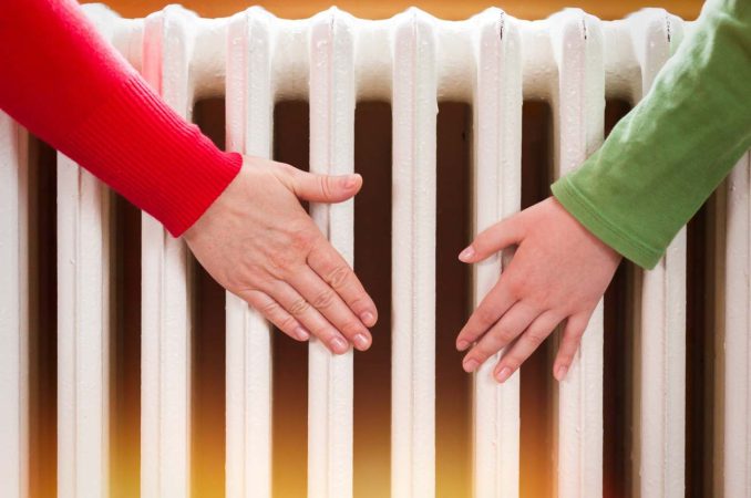 Deux mains placées près d'un radiateur blanc pour se réchauffer, illustrant quel chauffage d appoint choisir pour la maison.